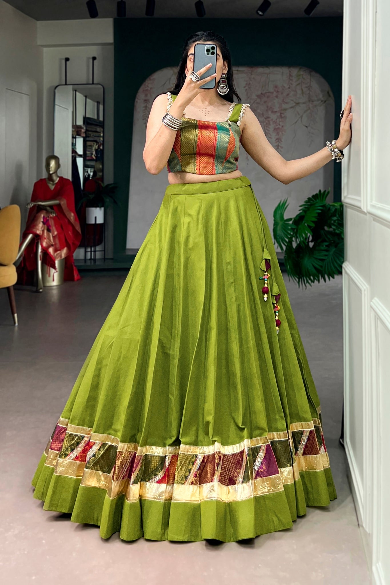 Woman wearing a parrot green traditional outfit with a colorful top, standing in a room.