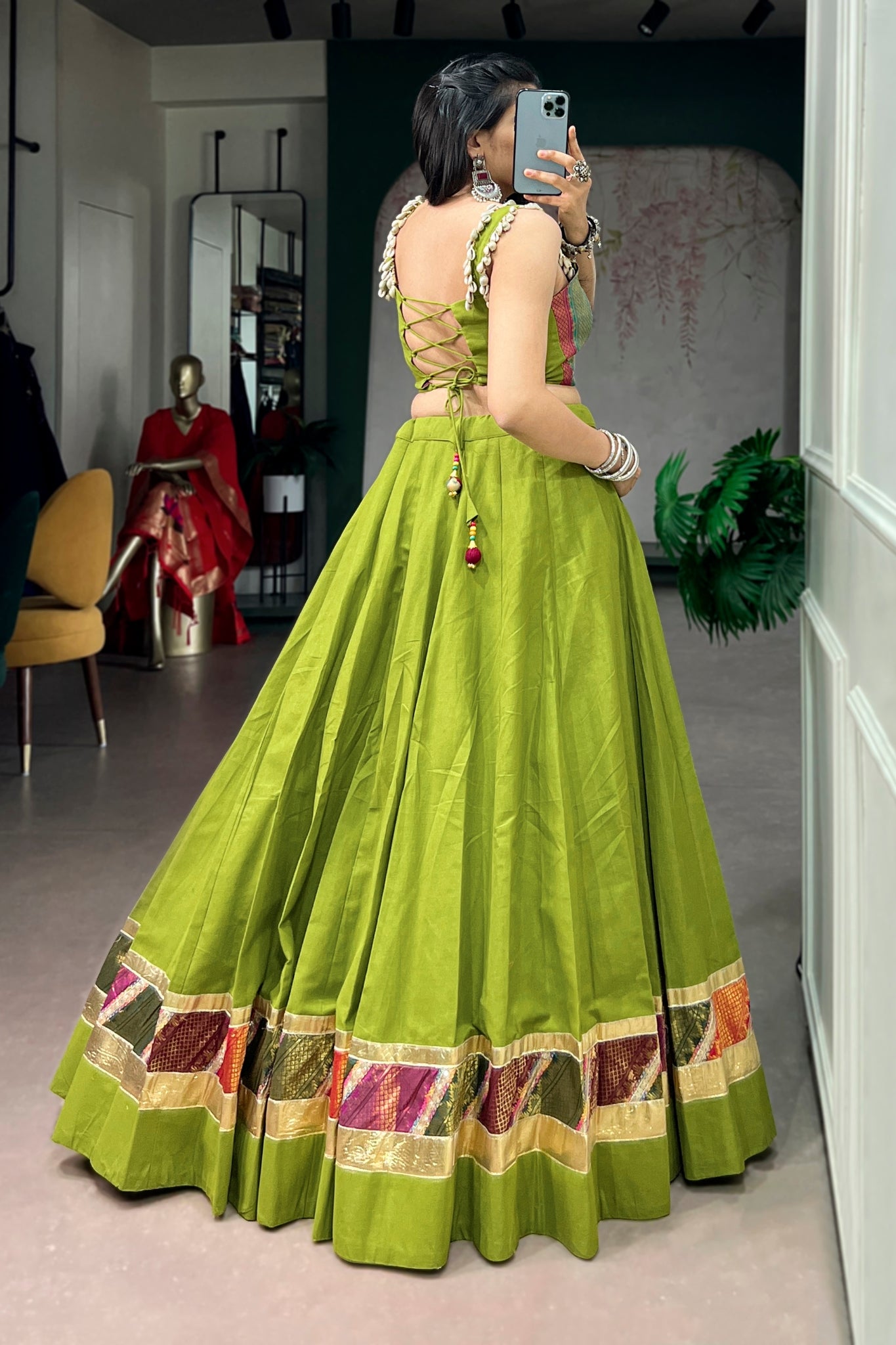 Woman in a parrot green traditional dandiya outfit with intricate designs, standing in a room.