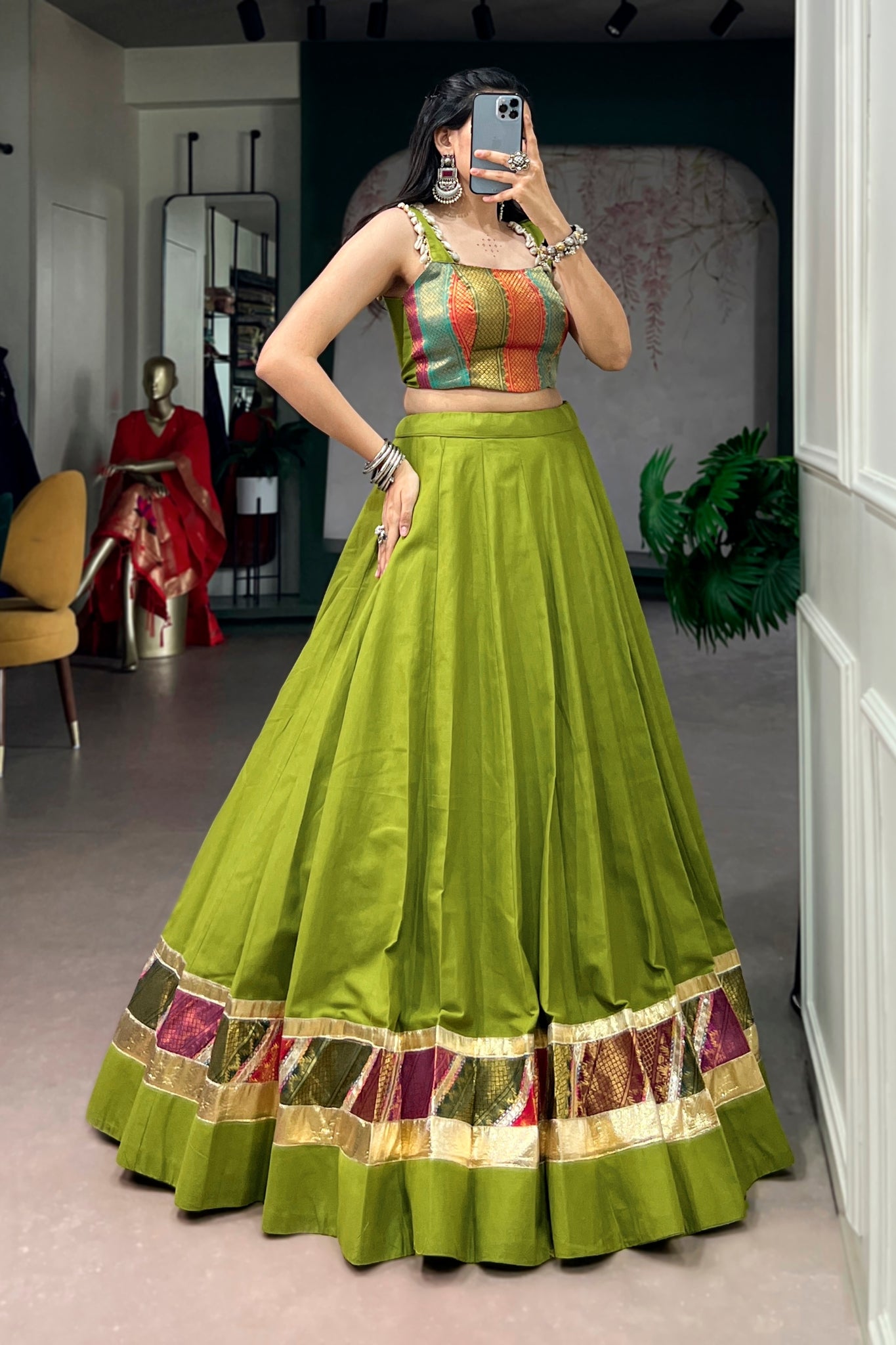 Woman in a parrot green traditional navratri outfit with colorful top, standing in a room.