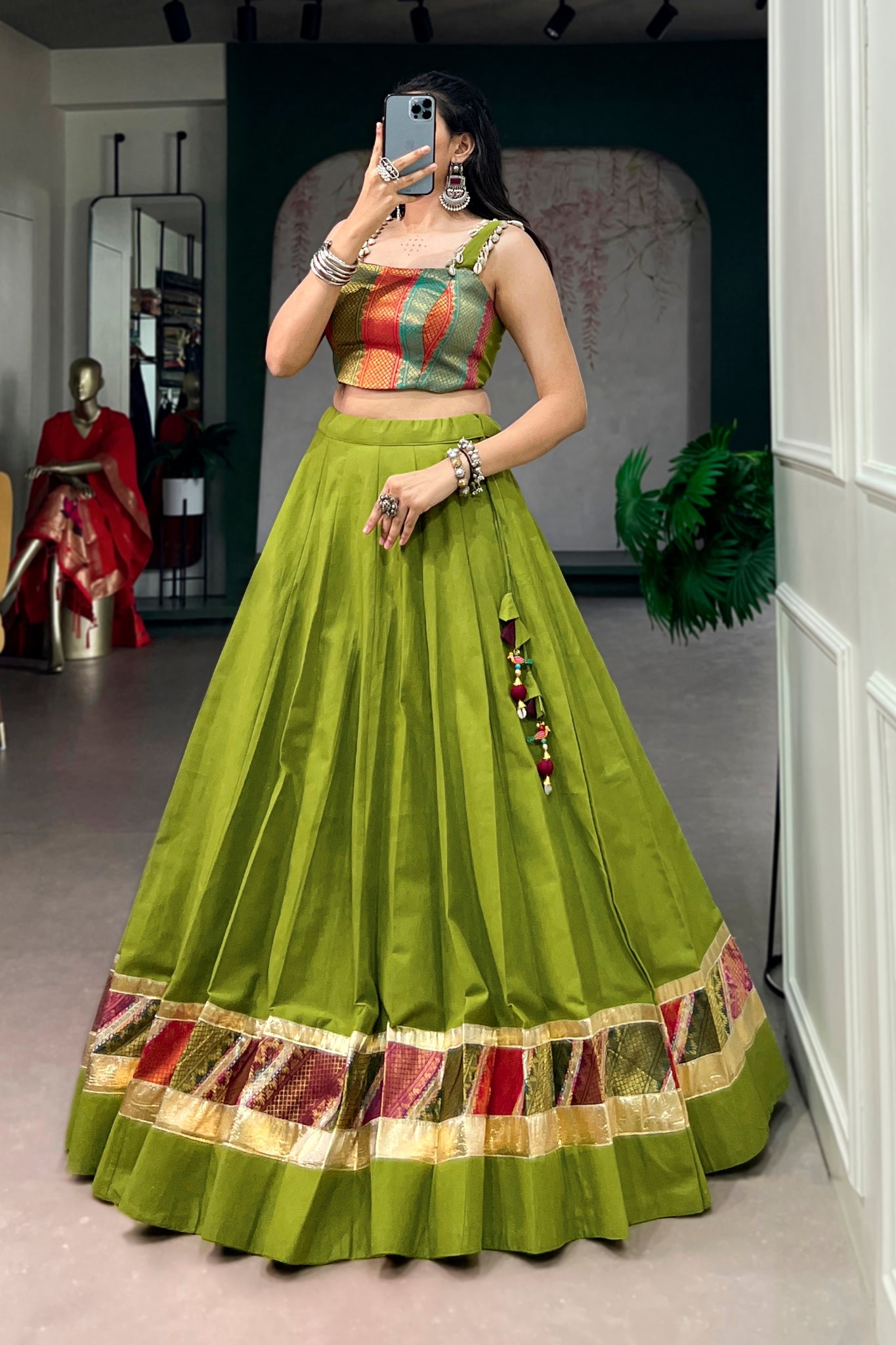 Woman taking a mirror selfie wearing a parrot green traditional garba outfit with colorful patterns.