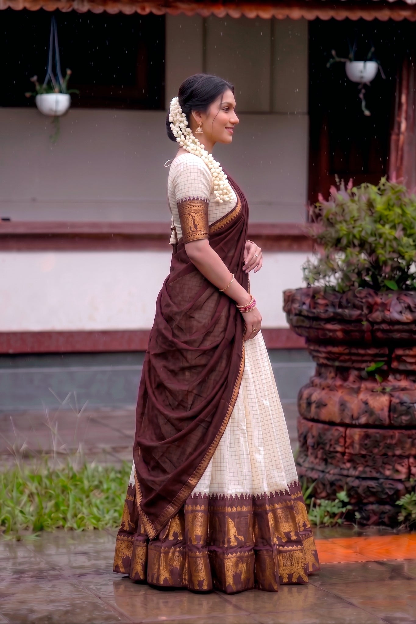 Woman in a traditional brown and white lehenga choli standing outdoors.