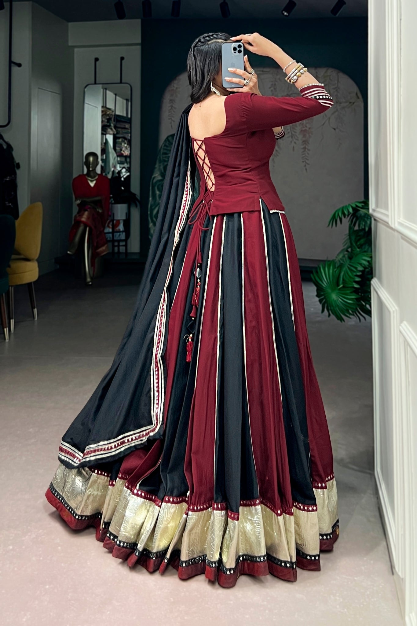 Woman in a maroon and black lehenga choli taking a mirror selfie in a room.