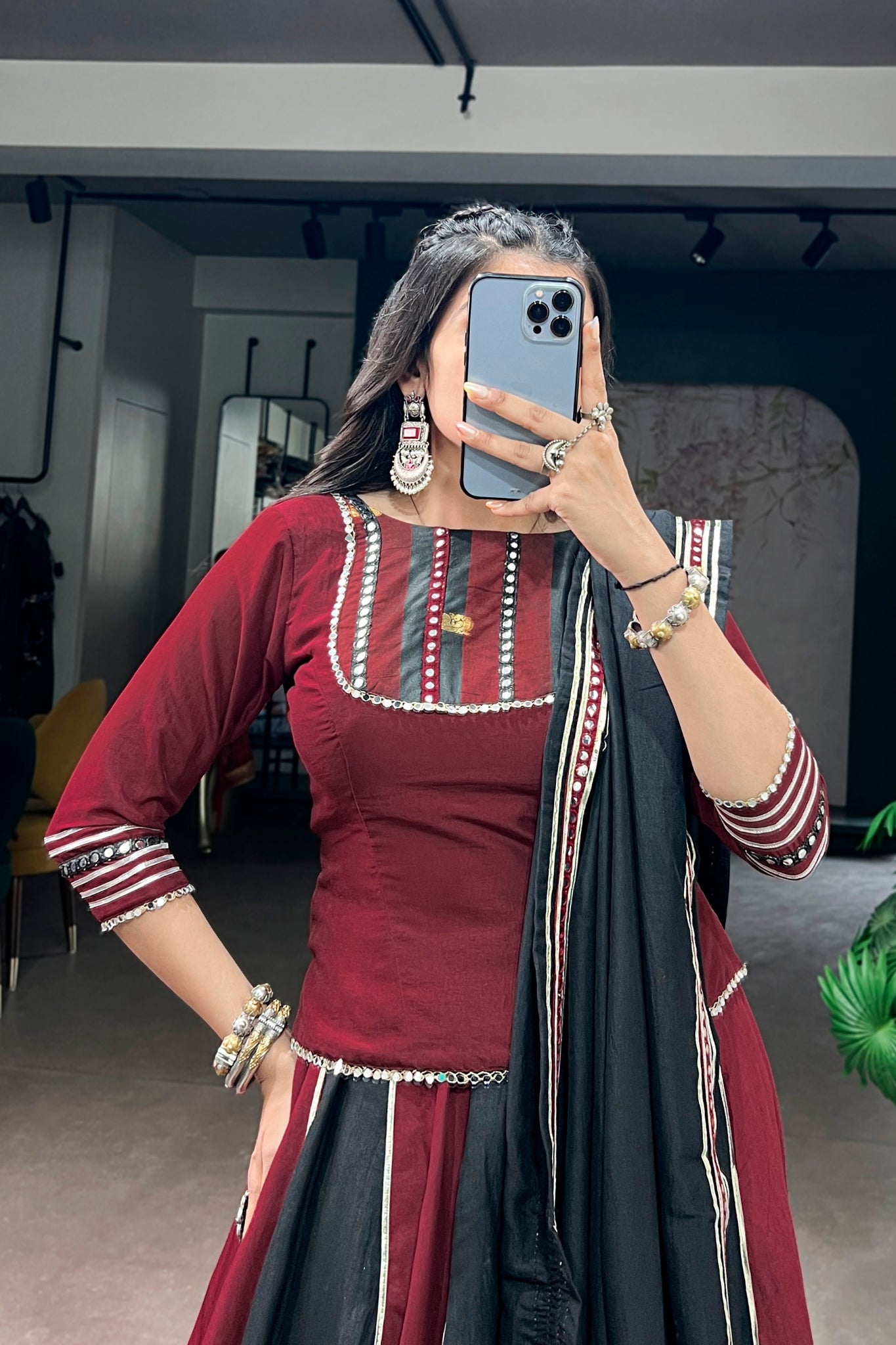 Woman taking a mirror selfie wearing a traditional garba outfit with a maroon blouse and black dupatta.