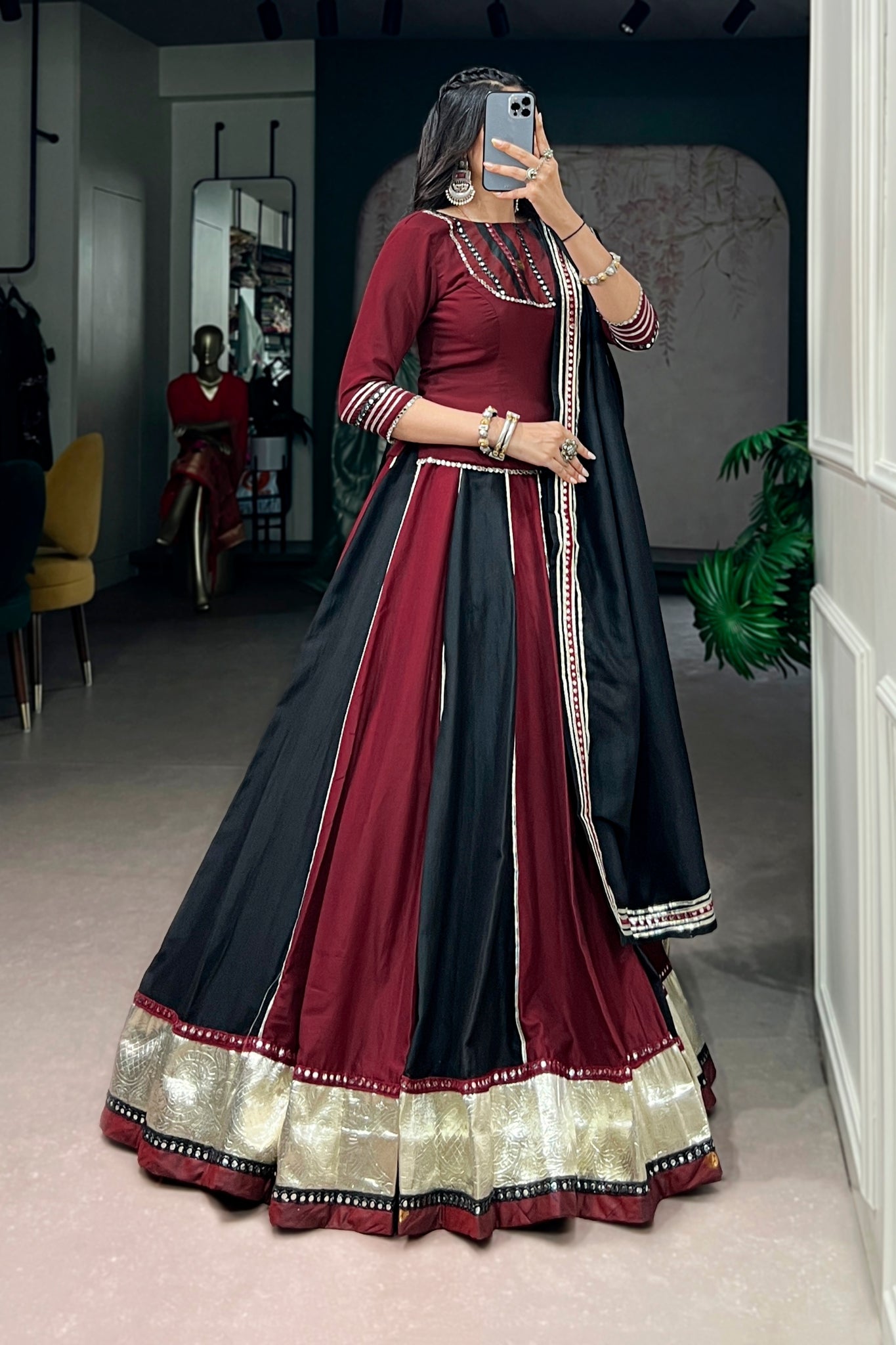 Woman taking a mirror selfie wearing a maroon and black traditional outfit 