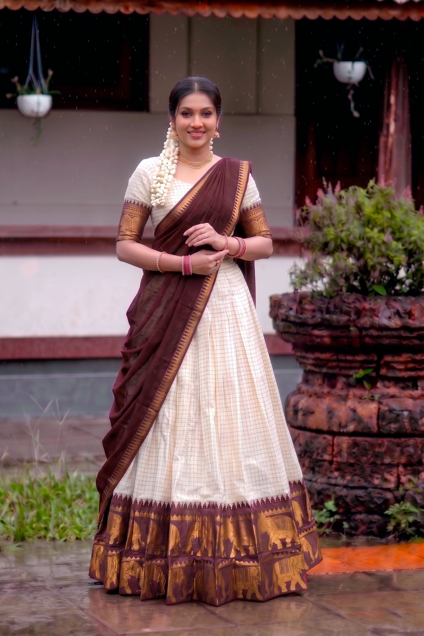 Woman in a traditional brown and white lehenga choli standing outdoors.