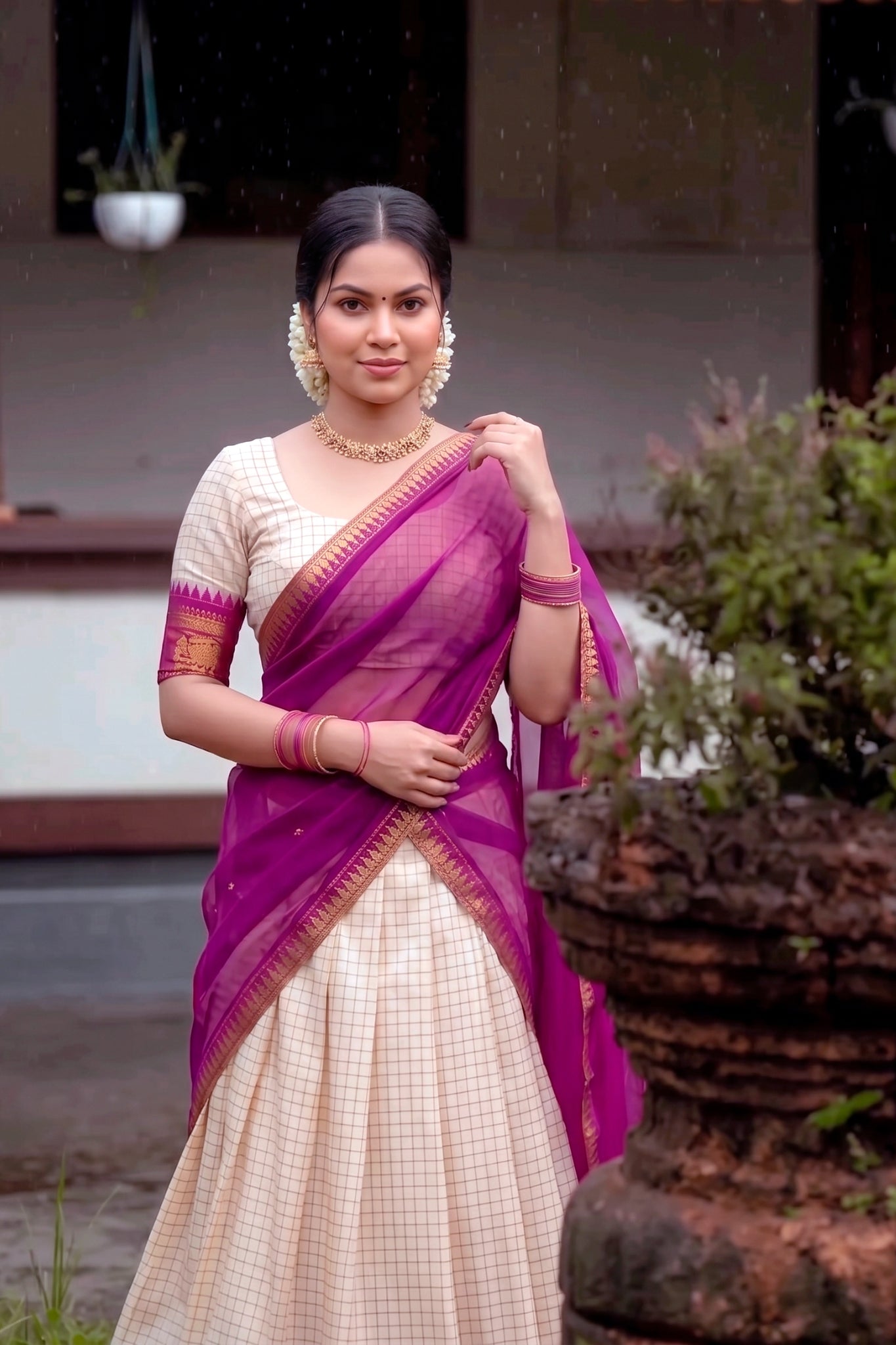 Woman in a traditional outfit with a wine lehenga and white blouse, standing outdoors.