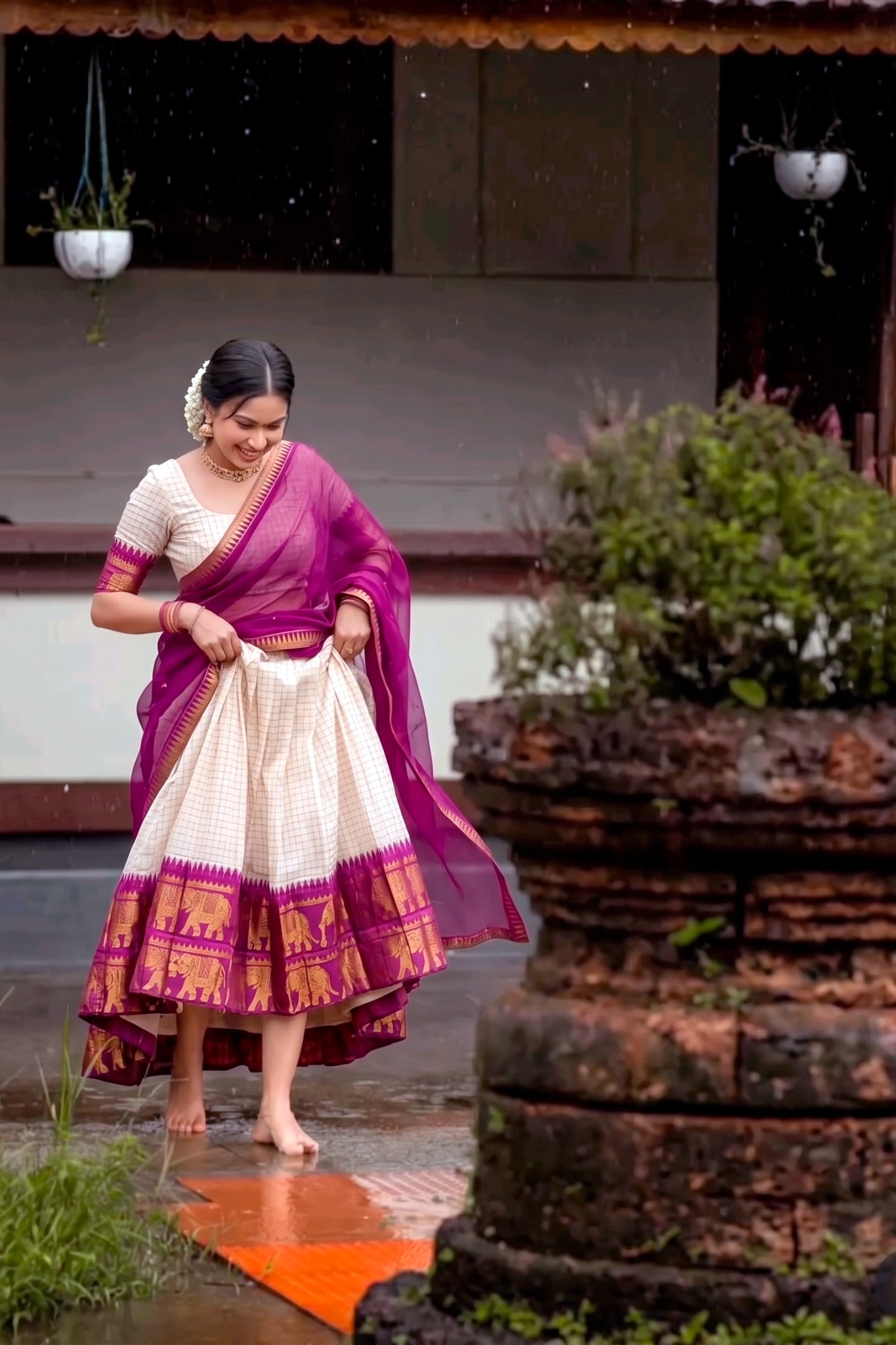 Woman in a traditional lehenga walking outdoors near a stone structure.
